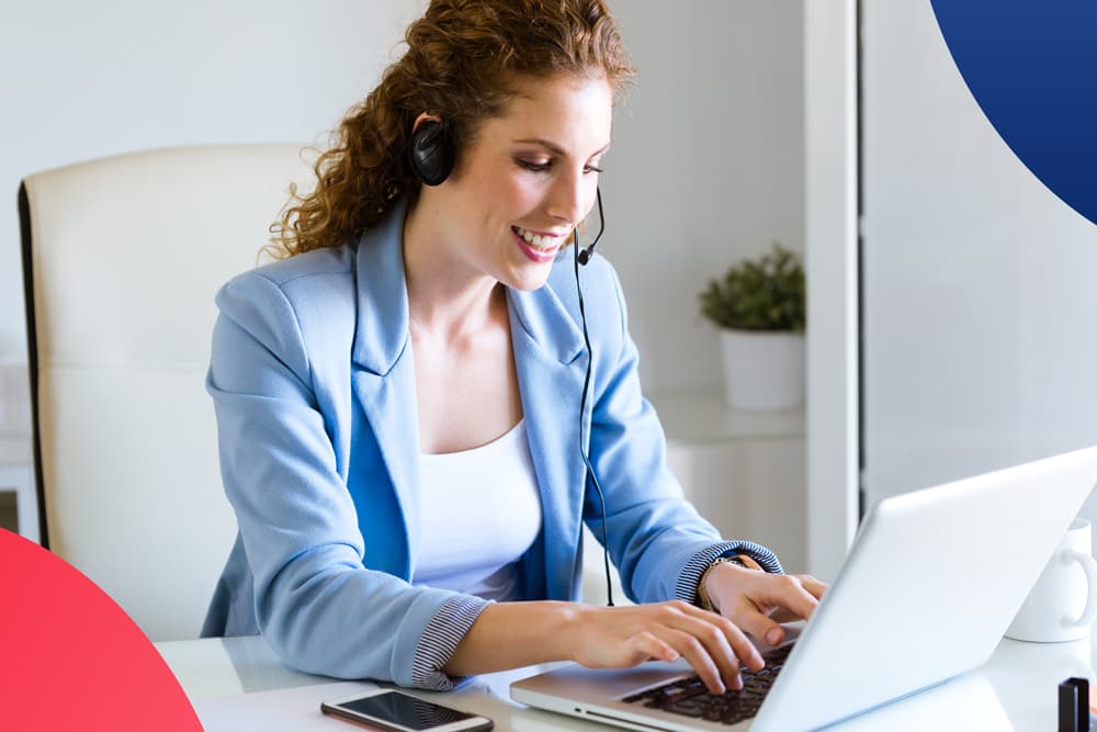 Un'operatrice del supporto clienti con cuffie e microfono sorride mentre lavora al computer